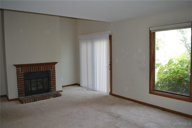 unfurnished living room with a healthy amount of sunlight, a brick fireplace, baseboards, and carpet flooring