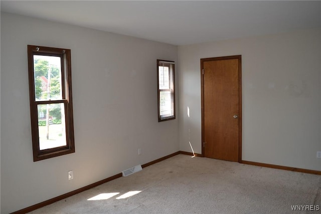 unfurnished room with light colored carpet, a healthy amount of sunlight, visible vents, and baseboards