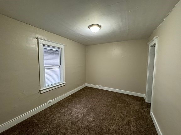 unfurnished room with baseboards and dark colored carpet