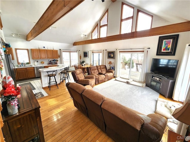 living room featuring high vaulted ceiling, light wood-style flooring, rail lighting, and beam ceiling