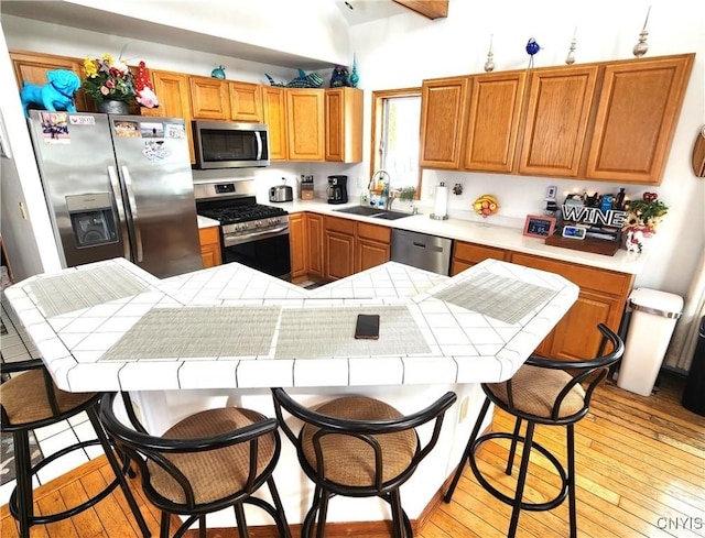 kitchen featuring light wood-style flooring, stainless steel appliances, a kitchen island, a sink, and a kitchen breakfast bar