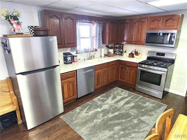 kitchen with dark wood finished floors, decorative backsplash, stainless steel appliances, a paneled ceiling, and a sink