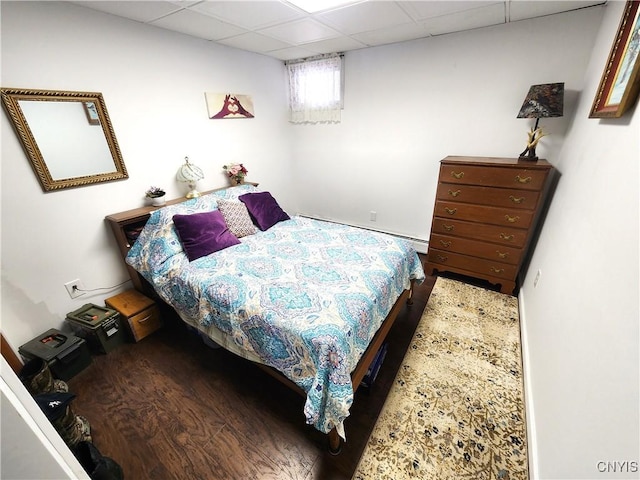 bedroom featuring baseboard heating, wood finished floors, and a paneled ceiling