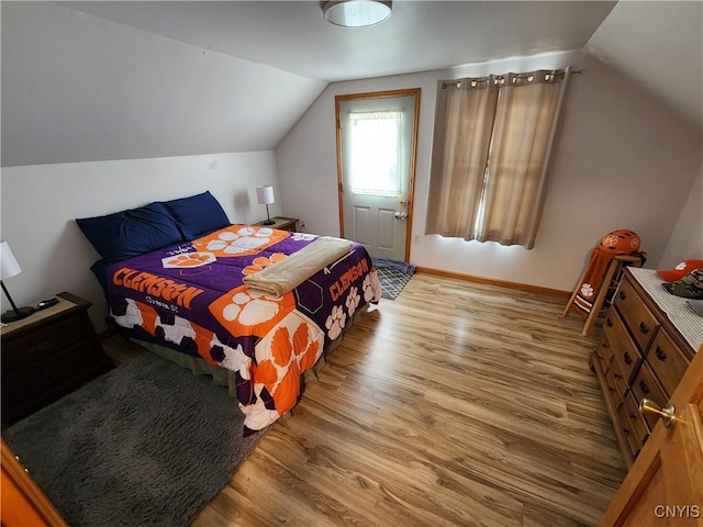 bedroom with vaulted ceiling, wood finished floors, and baseboards