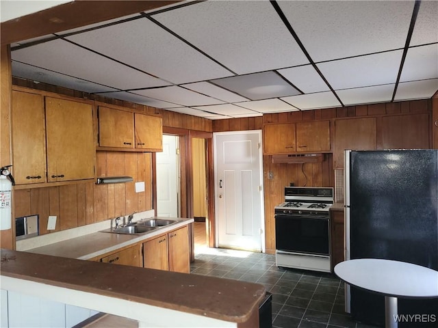 kitchen with brown cabinetry, gas range, freestanding refrigerator, a peninsula, and a sink