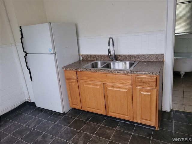 kitchen with dark tile patterned flooring, dark countertops, a sink, and freestanding refrigerator