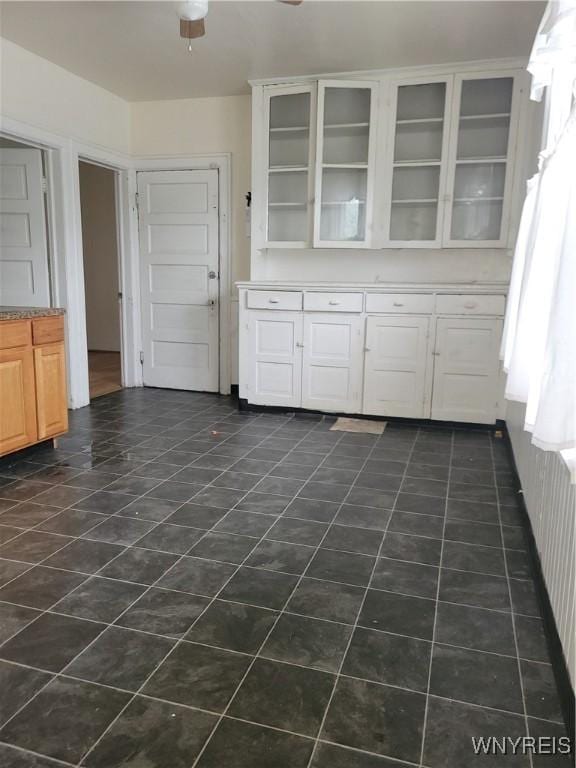 kitchen with glass insert cabinets, white cabinets, a ceiling fan, and dark tile patterned flooring