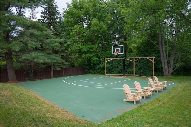 view of basketball court featuring basketball hoop, a lawn, and fence