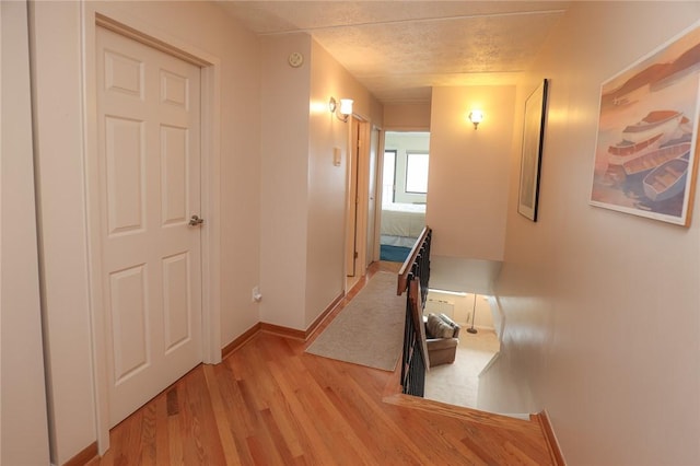 hallway with baseboards, a textured ceiling, and light wood finished floors