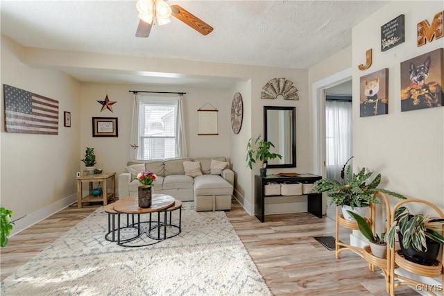 living area with light wood-type flooring, a ceiling fan, baseboards, and a textured ceiling