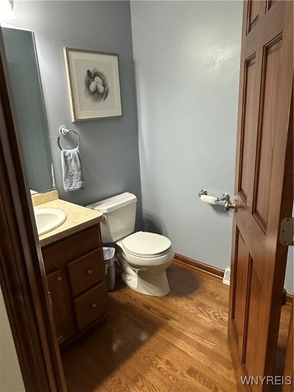 half bathroom with vanity, wood finished floors, toilet, and baseboards