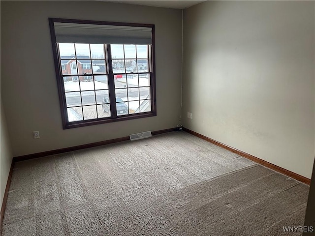 empty room with carpet floors, visible vents, plenty of natural light, and baseboards