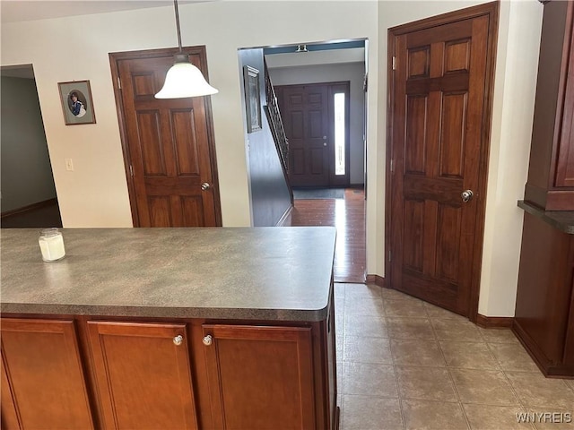 kitchen with baseboards, dark countertops, brown cabinets, hanging light fixtures, and tile patterned flooring