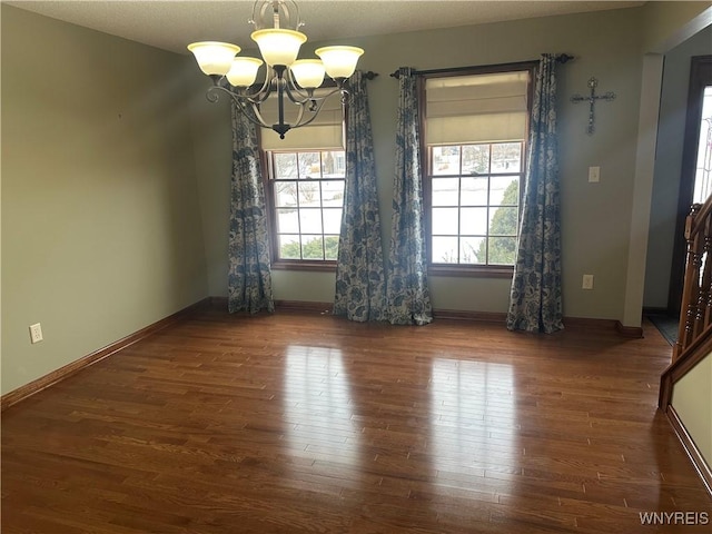 unfurnished dining area featuring baseboards, wood finished floors, and a notable chandelier