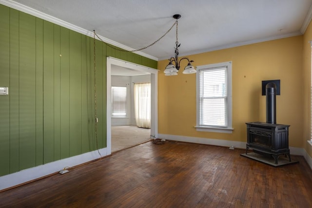 unfurnished dining area featuring hardwood / wood-style floors, an inviting chandelier, ornamental molding, a wood stove, and baseboards