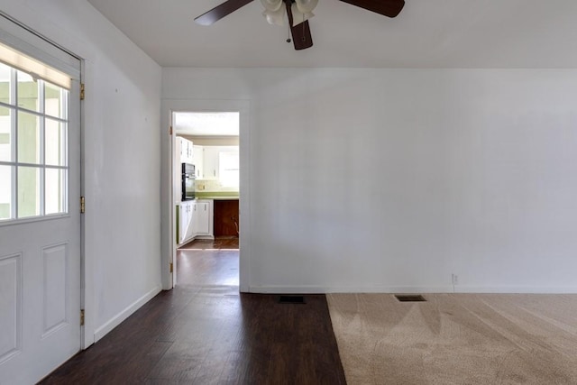 empty room with a ceiling fan, visible vents, baseboards, and dark wood-style flooring