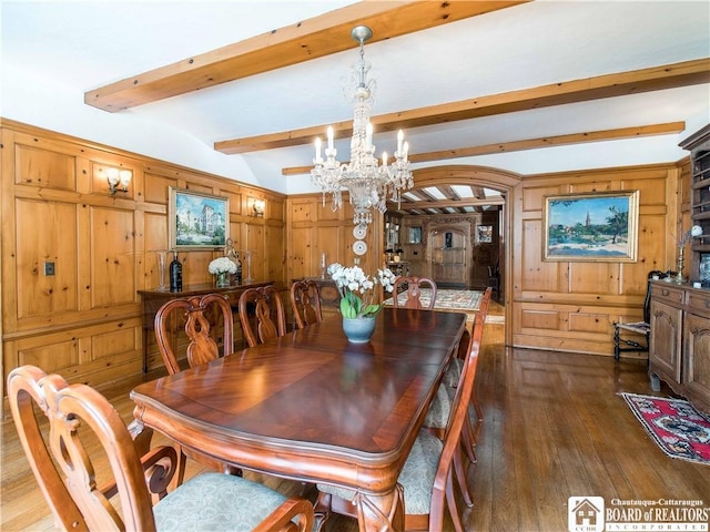 dining space featuring vaulted ceiling with beams, hardwood / wood-style flooring, wood walls, and an inviting chandelier