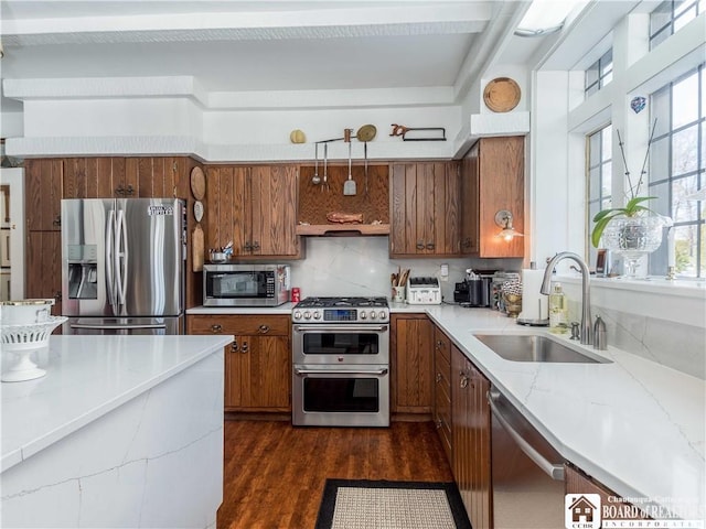 kitchen with decorative backsplash, appliances with stainless steel finishes, brown cabinets, dark wood-type flooring, and a sink