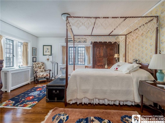 bedroom with multiple windows, wallpapered walls, radiator heating unit, and wood finished floors