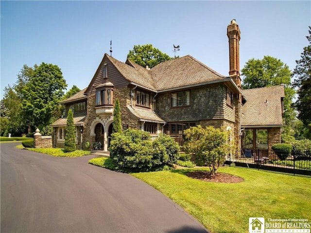 view of front of home with driveway, fence, a chimney, and a front lawn