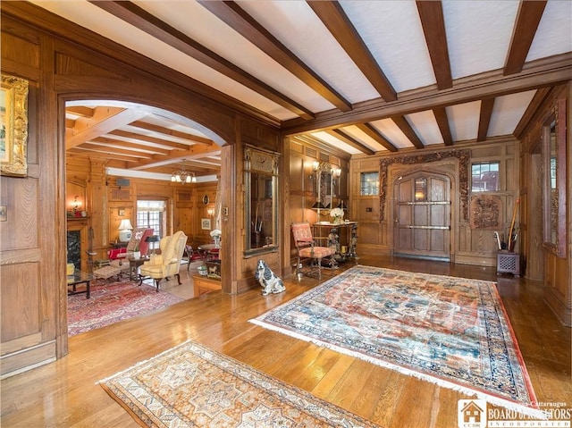 entrance foyer with wooden walls, arched walkways, beam ceiling, and wood finished floors