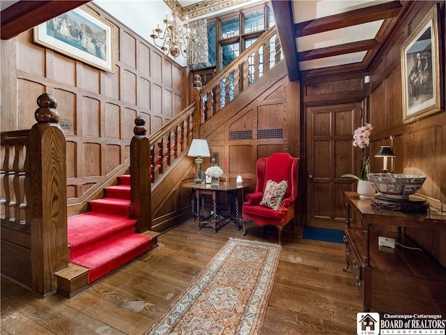 interior space featuring beam ceiling, wood-type flooring, a decorative wall, wood walls, and a chandelier