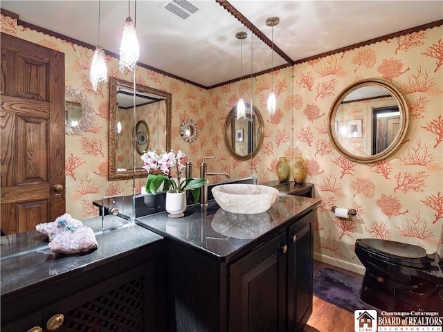 bathroom featuring visible vents, vanity, wood finished floors, baseboards, and wallpapered walls