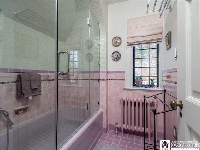 full bath featuring tile patterned flooring, shower / bath combination with glass door, tile walls, wainscoting, and radiator heating unit