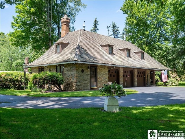 view of front of house featuring aphalt driveway, stone siding, a front lawn, a chimney, and a high end roof