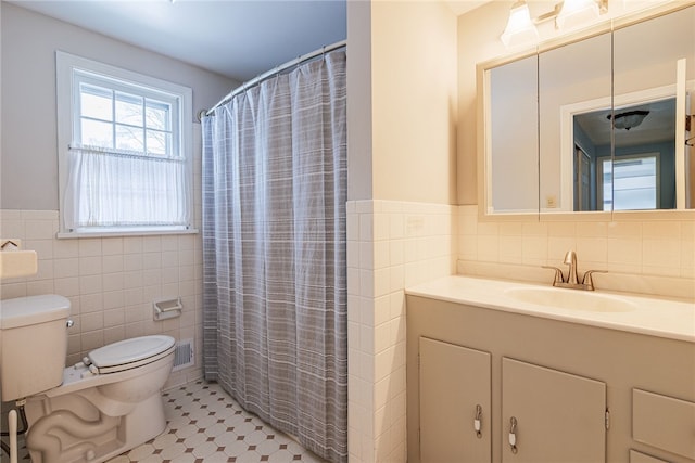 bathroom with toilet, a wainscoted wall, a shower with shower curtain, vanity, and tile walls