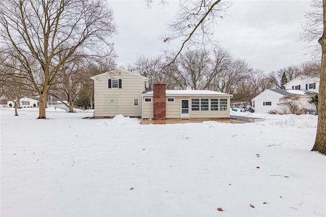 snow covered rear of property with a chimney and a sunroom