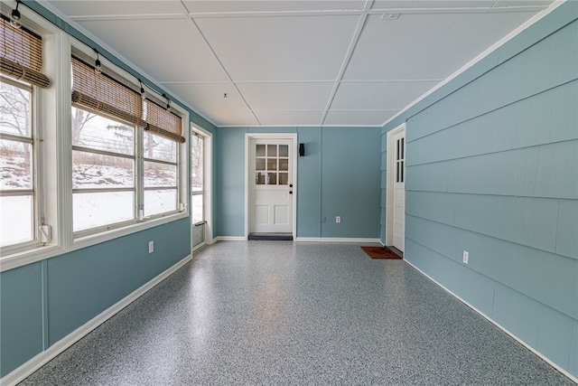 spare room featuring speckled floor, a drop ceiling, a wealth of natural light, and baseboards