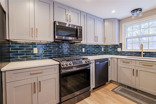 kitchen with stainless steel appliances, tasteful backsplash, light countertops, gray cabinetry, and a sink