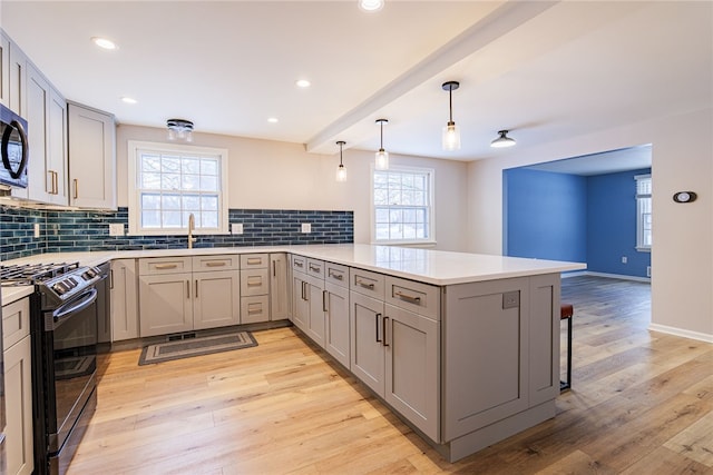 kitchen featuring a peninsula, light wood-style floors, backsplash, gray cabinets, and gas stove