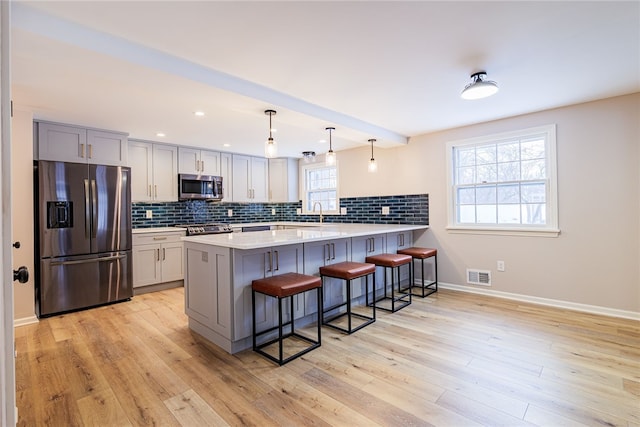 kitchen featuring stainless steel appliances, visible vents, backsplash, a peninsula, and a kitchen bar