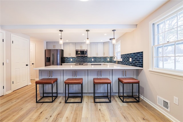 kitchen with visible vents, a peninsula, stainless steel appliances, a kitchen bar, and a sink