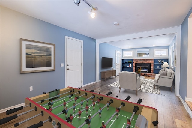 game room featuring hardwood / wood-style floors, track lighting, a brick fireplace, and baseboards