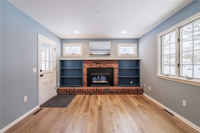 unfurnished living room with wood-type flooring, visible vents, a fireplace, and baseboards