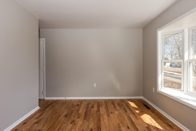 unfurnished room with wood finished floors, visible vents, and baseboards