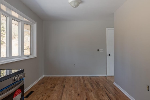 empty room with wood finished floors, visible vents, and baseboards