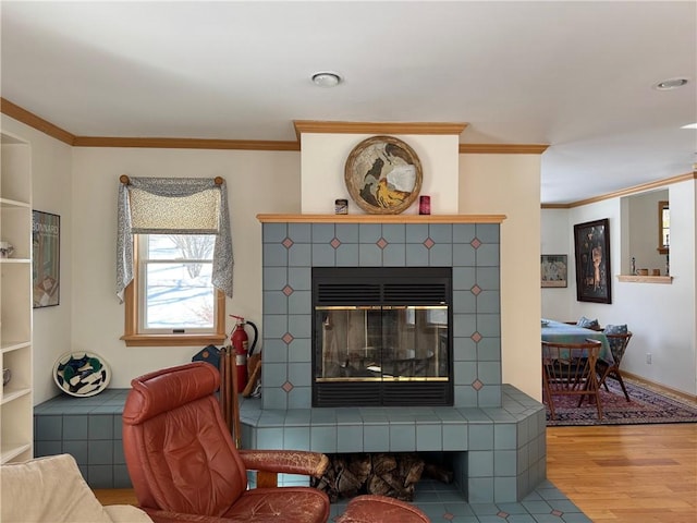 living room featuring baseboards, crown molding, a tiled fireplace, and wood finished floors