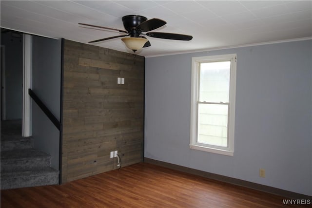 empty room with ornamental molding, ceiling fan, baseboards, and wood finished floors