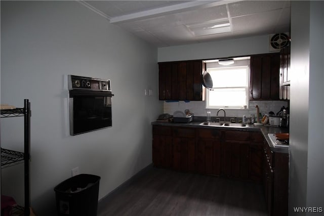 kitchen with dark wood-style floors, tasteful backsplash, a sink, dark brown cabinets, and black oven