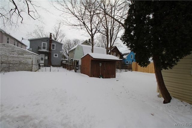 yard layered in snow with a storage shed, fence, and an outbuilding