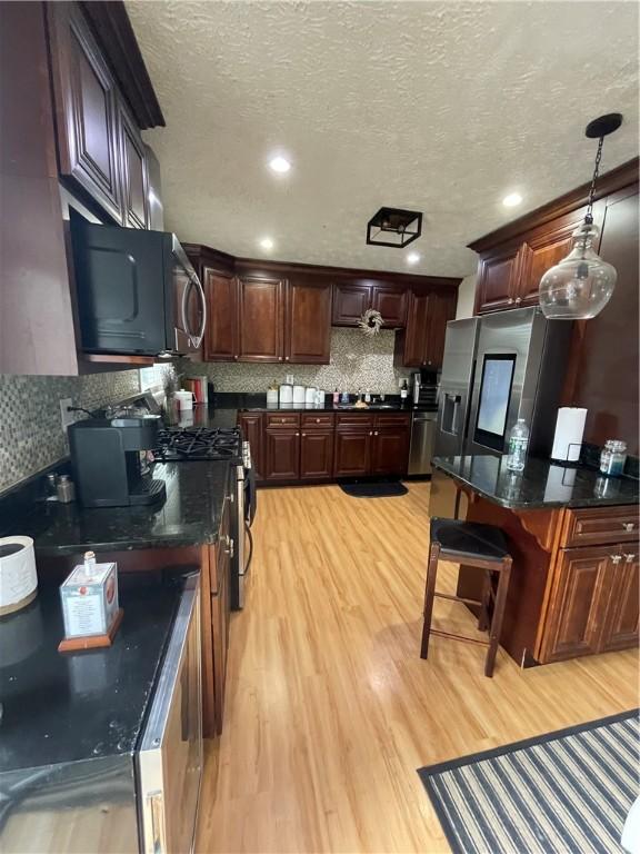 kitchen with pendant lighting, appliances with stainless steel finishes, light wood-type flooring, and tasteful backsplash