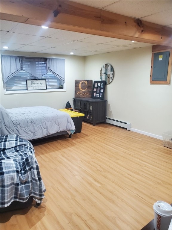 bedroom with electric panel, baseboards, wood finished floors, a paneled ceiling, and a baseboard heating unit