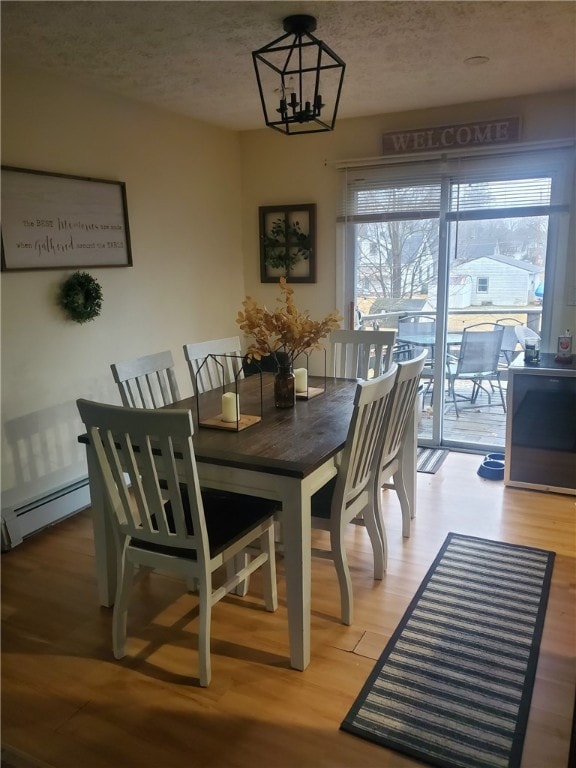 dining area featuring an inviting chandelier, light wood finished floors, baseboard heating, and a textured ceiling