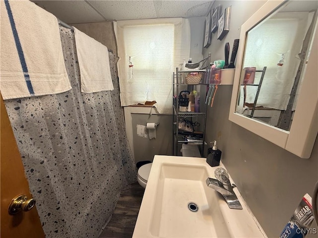 full bath featuring a drop ceiling, toilet, a shower with curtain, wood finished floors, and a sink