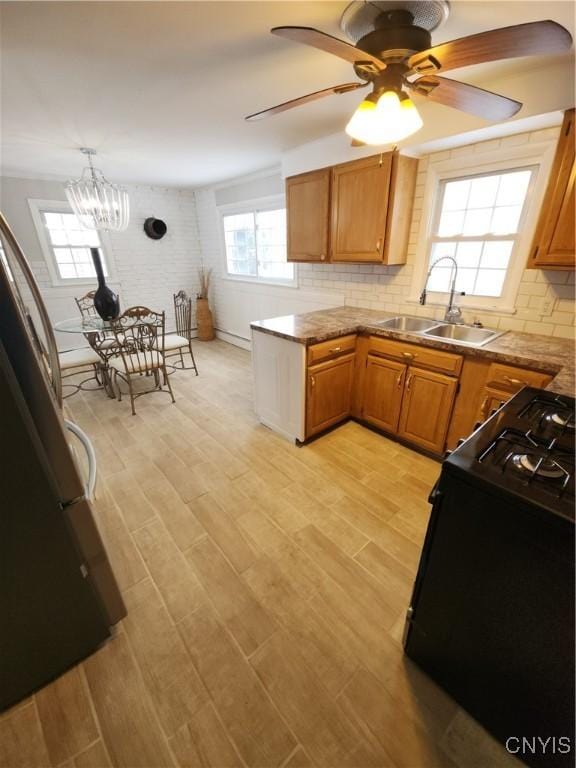 kitchen featuring tasteful backsplash, light wood finished floors, brown cabinetry, black appliances, and a sink