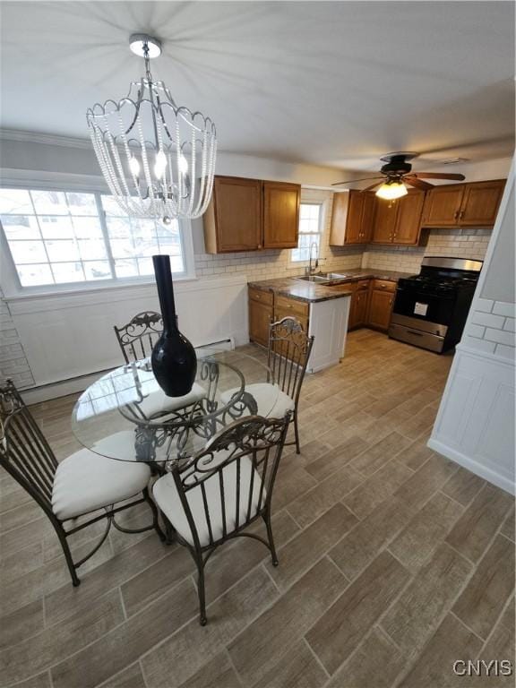 dining area with ceiling fan with notable chandelier, wood finish floors, baseboard heating, and crown molding